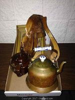 Copper tea pot, ceramic Japan tea pot, wooden shoe wine bottle holder with hanger, and two framed prints all displayed together in a box.