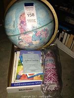 Photo of Replogle globe showing map of North and South America, box with flashcards and reference books, and teacher water bottle in packaging