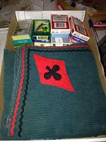 Photo showing multiple vintage and modern playing card decks including Budweiser branded decks, displayed on a vintage dark green corduroy card suit themed tablecloth with red diamond and club suit design and rickrack trim.