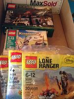 Photo showing four LEGO kits stacked in a box including LEGO Hobbit, Kingdoms, and two sealed LEGO train sets with The Lone Ranger set in front