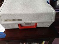 Closed view of the white textured case with red handle and GE branding on the lid.