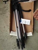 Ambico tripod folded and placed in a cardboard box with MaxSold tag showing.