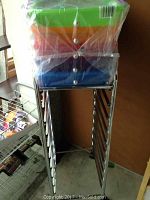 Photo showing stacked colored plastic drawers (green, orange, red, purple, blue) wrapped in plastic on top of metal frame.