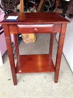Full front view of the wood side table showing one drawer and lower shelf, placed in garage-like space.