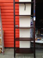 Full view of tall, dark wood veneer ladder shelf with five shelves and wall strap.