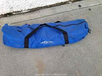 Closed blue carrying case with black handles on pavement, showing wear and dirt