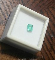 Loose rectangular step cut green emerald displayed in a white plastic gem box on a wood surface