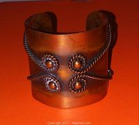 Front view of mid century copper bangle bracelet with twisted copper wire and round copper accents on an orange background.