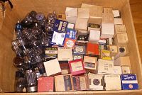 Top view of a cardboard box filled with vintage electronic tubes and their original packaging boxes, showing a variety of sizes and brands.