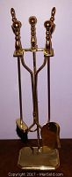 Full view of polished solid brass fireplace tool set with stand, containing poker, brush, and shovel.
