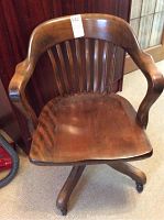 Front view of wooden swivel desk chair showing curved arms, slat back and five-legged base with caster wheels