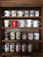 Shelf with four rows of assorted mugs, including commemorative and floral designs