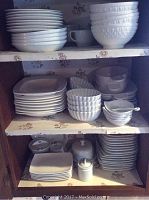Three-shelf cabinet filled with stacks of white plates and bowls