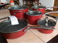 Full set of red KitchenAid pots and pans displayed on a table showing all items with handles and lids