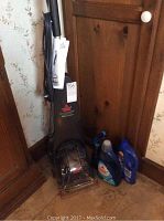 Full view of Bissell QuickSteamer upright carpet cleaner with handle and cleaning head. Three bottles of cleaning solution placed beside it.