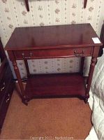 Front view of the wooden occasional table showing the tabletop, drawer with metal handles, turned legs, and lower shelf.
