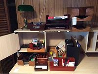 Wide view of desk surface showing paper shredder, wooden trays, and organizing containers with office supplies.