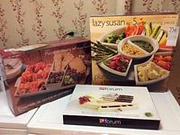 Photo of all three boxed serving sets stacked on a white surface against floral wallpaper.