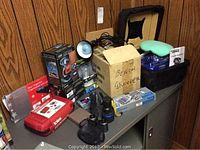 Overview of various car-related items on a metal cabinet including boxed bench grinder, emergency kit, visor organizer, clip-on fans, and polisher.
