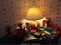 Overall view of the lamp, wooden candle holders, candles and night light on a table against a floral wallpaper.