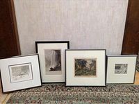 Four framed decorative prints displayed leaning against a wall on a carpet. Frames in black with white mats. Various nature scenes including winter and forests.