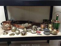 Shelf with assorted metal and copper decorative items including candelabra, pots, planters, bell, and coins