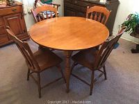 Round maple kitchen/dining table with four chairs around it, showing the table top and legs.