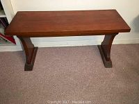 Front angled view of the pine bench showing rectangular seat and sturdy base with curved supports.