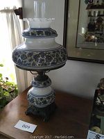 Full view of the oil lamp showing ceramic base and paisley design with glass chimney on top.