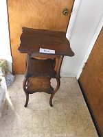 Full view of the carved oak stand showing three tiers with carved edges, curved legs, and side beading detail.