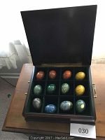 Closed wooden case with lid open showing 12 polished alabaster eggs in compartments, various colors including red, green, blue, yellow, and gray.