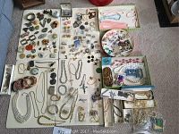 Overview of the entire lot laid on multiple white tables showing variety of jewelry including necklaces, bracelets, rings, brooches, and earrings.