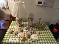 Photo showing both sea shell lamps, large coral, sand dollars, and assorted shells on green checkered tablecloth