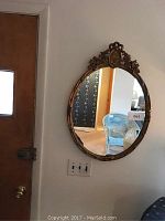 Oval gilded wall mirror hanging on wall in room, shows overall shape and setting.
