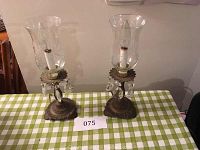 Full view of the pair of candlestick lamps on a checkered tablecloth, showing etched glass hurricane shades, ornate brass-style bases, and crystal prism drops.