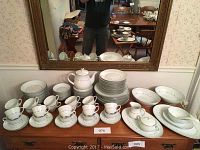 Full view of the 98 piece Noritake china set arranged on a wooden furniture piece, showing plates, cups, saucers, serving bowls, and teapot.