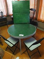 Green round folding card table with four black Samsonite folding chairs, chairs arranged around table.