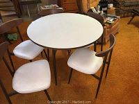 Full view of round white Formica table surrounded by five wood and metal chairs.