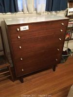 Front view of Bassett Furniture 4-drawer chest showing wood finish and white knob handles with white Formica top surface, situated indoors by windows and curtains.