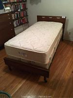 Full view of the twin bed frame with mattress and box spring, showing the wood finish and caster wheels.