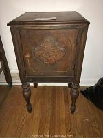 Front view of the vintage wooden smoking stand showing the closed door with decorative carved panel and turned legs.