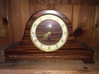 Wooden mantle clock with curved top, dark wood finish and circular face sitting on wooden surface.