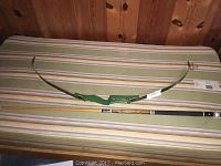 Full length view of the disassembled Bearcat take down bow and the 2-piece pool cue side by side on striped surface.