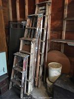 Four wooden step ladders of varying heights leaning against a wall in a storage area with visible wear and paint marks.