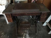Singer antique treadle sewing machine in wooden cabinet with top closed, showing for storage.