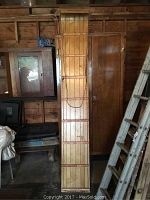 Full length view of wooden toboggan showing length and width, laid vertically in a wooden shed with other items around it.