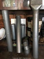 Various galvanized metal pipes, elbow duct pieces and flat sheets arranged upright against a wall and cabinet