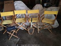 Four yellow canvas folding directors chairs, blue Rochester International folding golf stool, wooden baseball bat, and wooden tennis racket all visible in a dimly lit space.