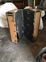 Opened antique steamer trunk showing side with four black drawers and metallic handles
