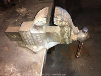 Front view of the large metal vise attached to a workbench, showing the jaws, handle, and mounting area.